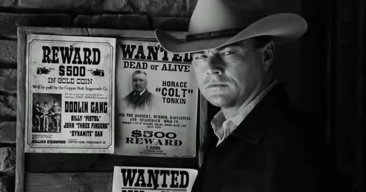 Rick Dalton as Jake Cahill in a cowboy hat stands in front of a bulletin board with Wanted posters