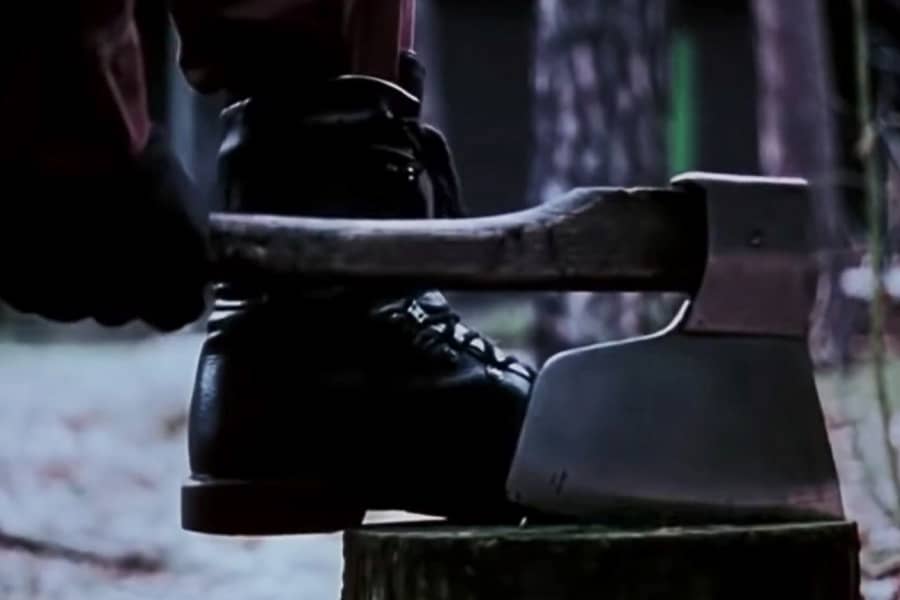 a man wearing a black boot pulls an axe from a stump
